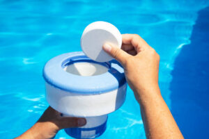 Hand Holding White Chlorine Tablet Over Swimming Pool Skimmer